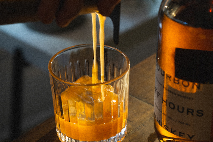 An old fashioned being poured into a glass with sunlight beaming