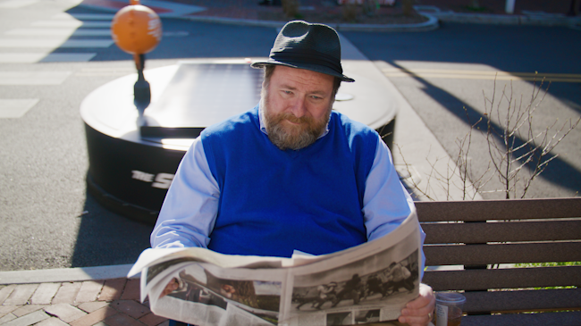A man sitting on a bench with a giant earth-cleaning robot passing behind him