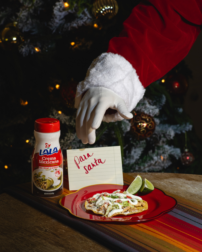 Santa reaching for a taco topped with Lala crema Mexicana