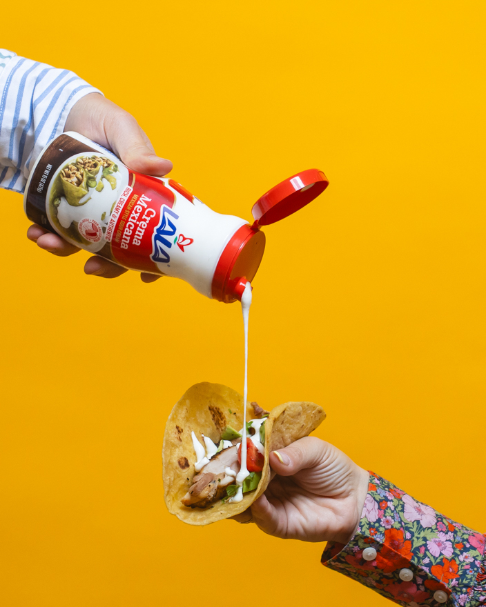 A taco being topped with Lala crema Mexicana