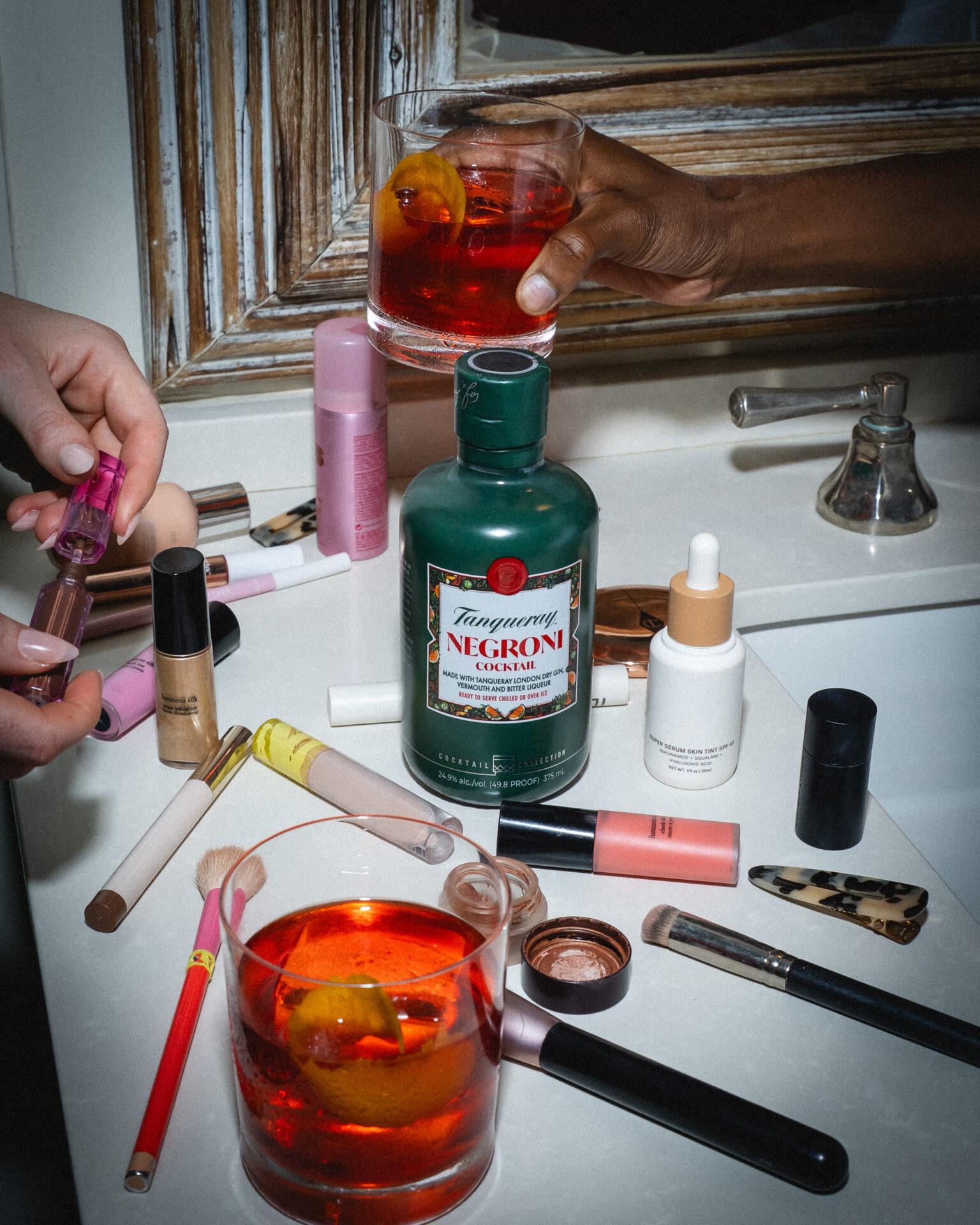 A bathroom counter with makeup products and drinks