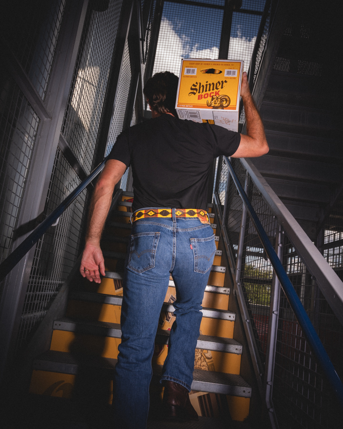 A man carrying a case of Shiner Beer up stairs